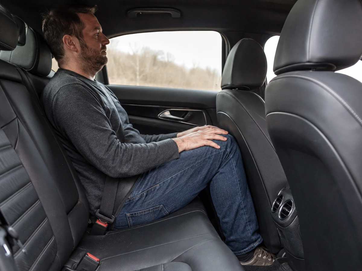Adult passenger seated behind a front seat set for a tall driver, knees close to the seatback, showing the rear legroom check - Cadillac CT4