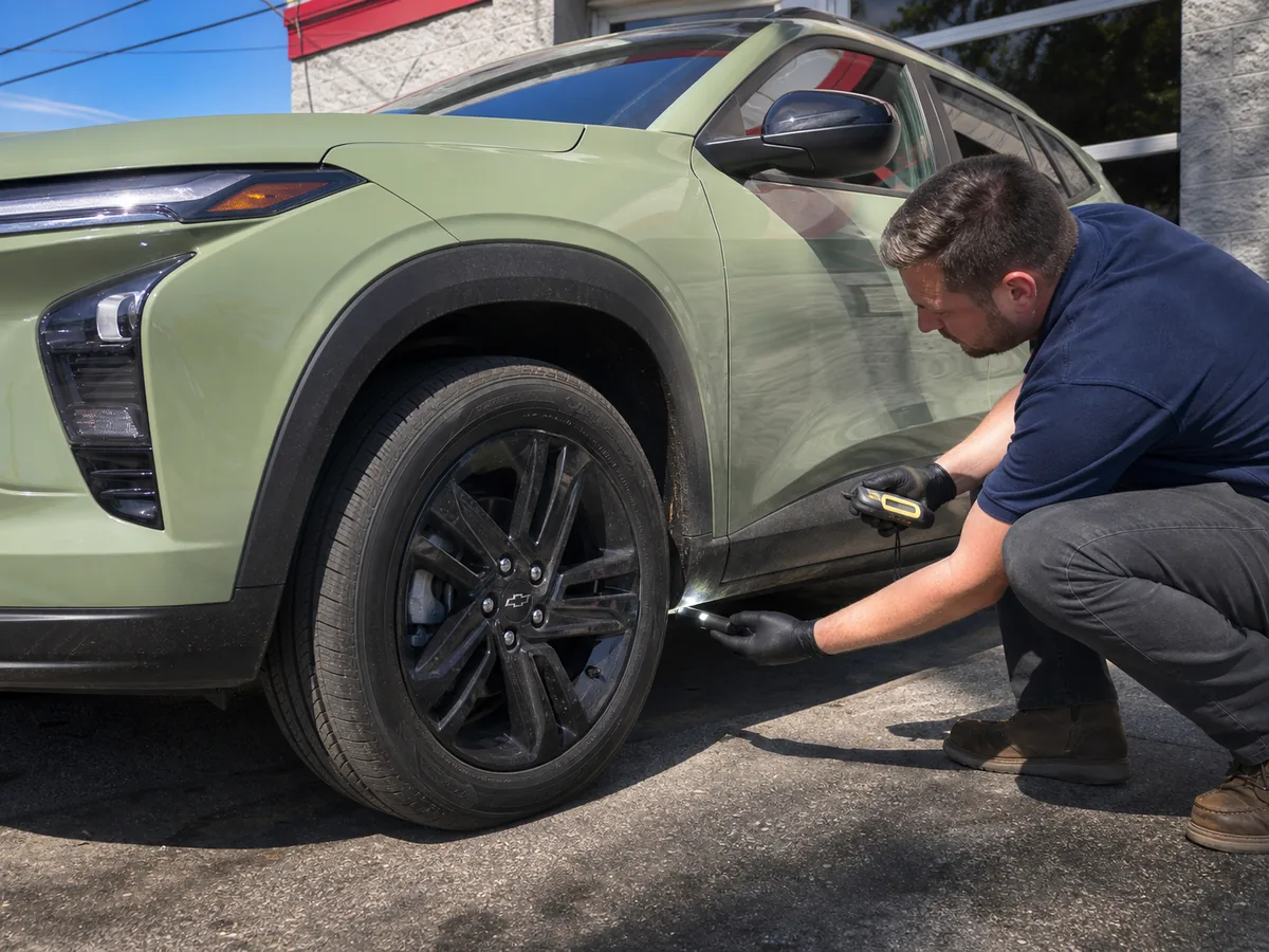 Technician checking Chevrolet Trax tire wear, lower body paint, and underbody condition outdoors