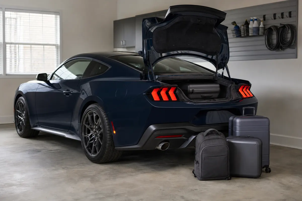 Ford Mustang fastback in a home garage with a work bag and two travel cases beside the open trunk