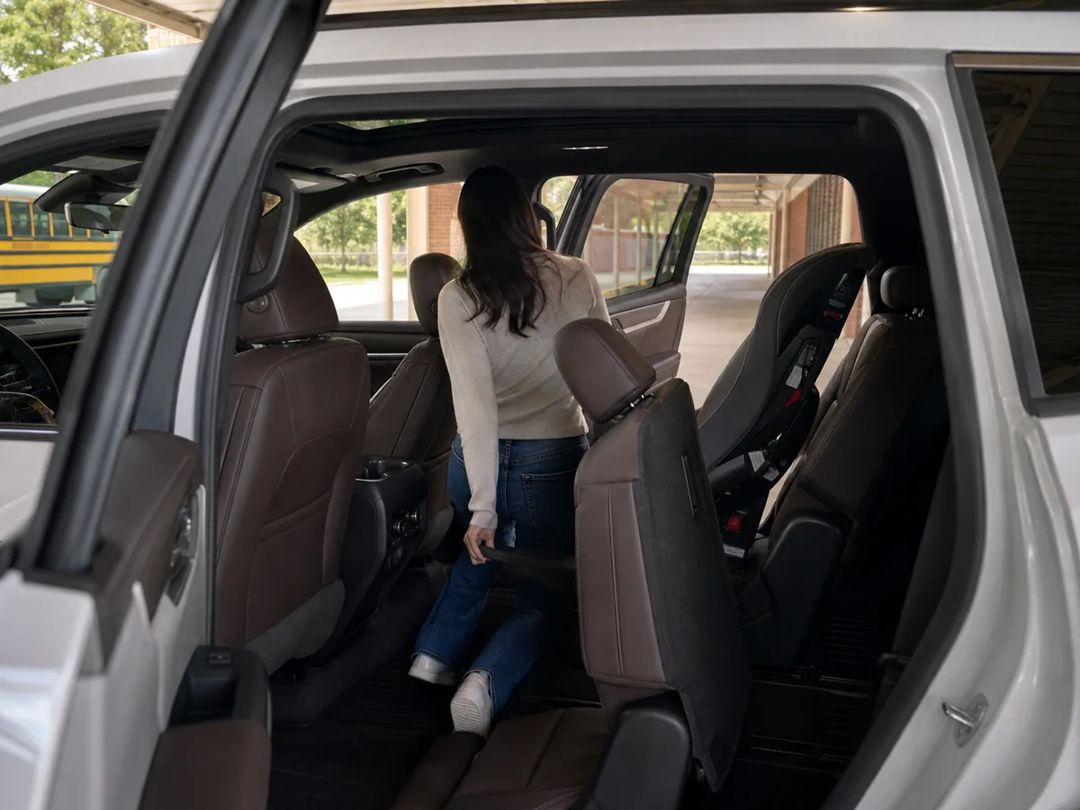 Adult entering the third row of a 2026 GMC Acadia with one second-row child seat installed - GMC Acadia