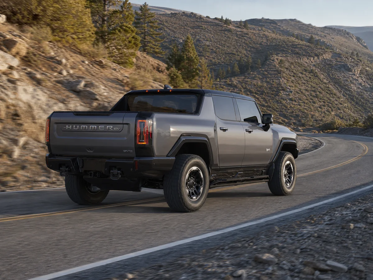 Gray GMC Hummer EV Pickup driving through a mountain-road bend from the rear three-quarter angle - GMC Hummer EV