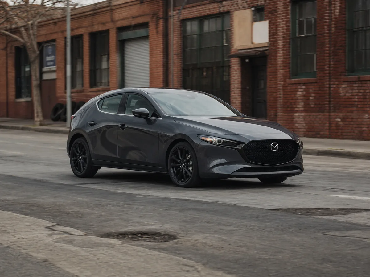 2026 Mazda3 hatchback driving on patched urban pavement during a buyer road test - Mazda3