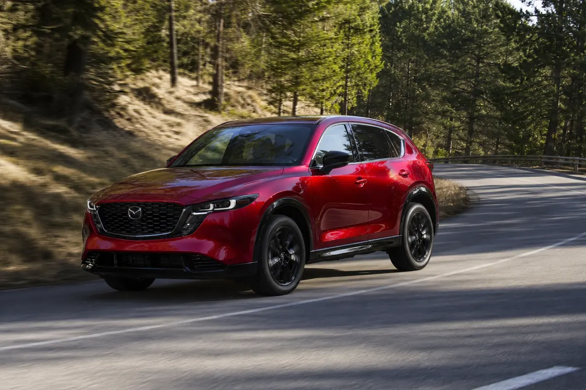 Mazda CX-5 tracking through a broad wooded-road bend in a front-side view