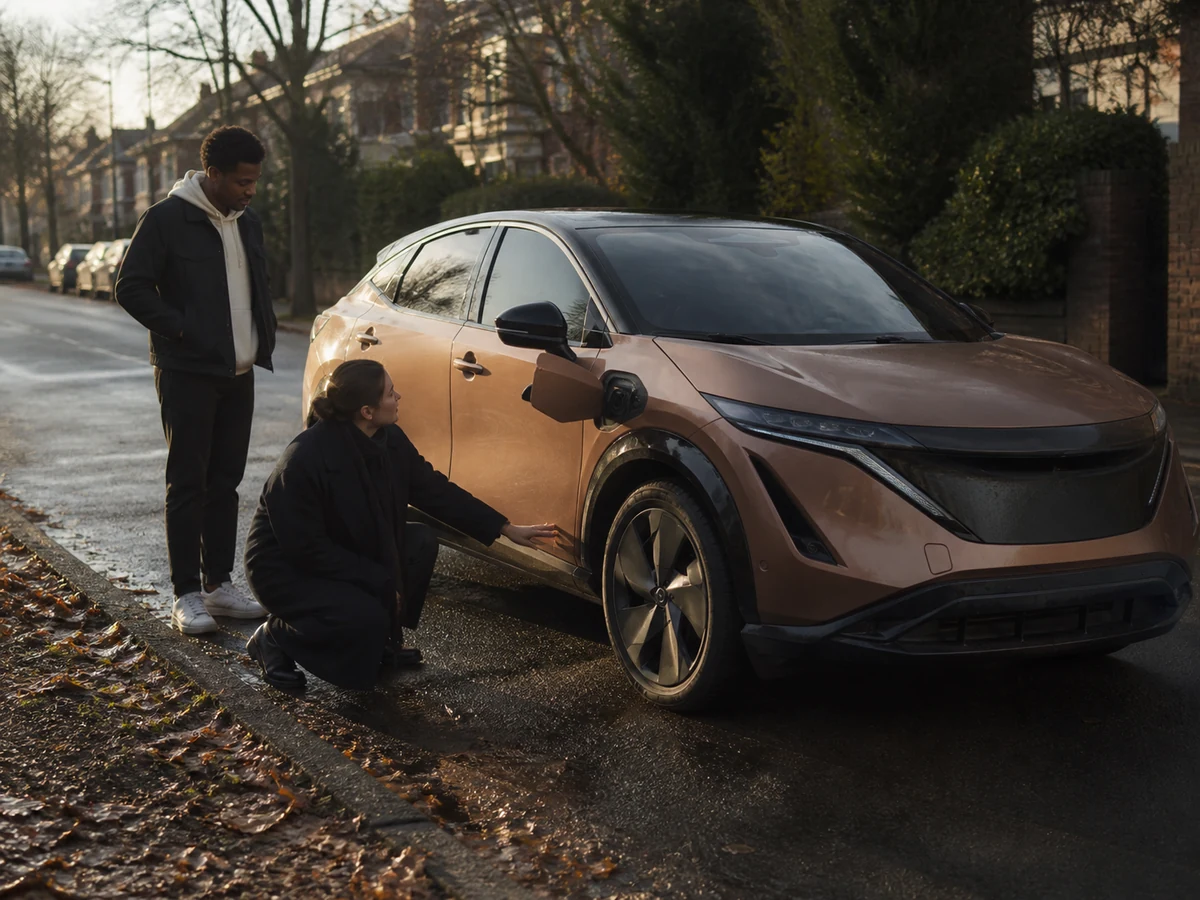Buyer crouched at the front wheel of a used Nissan Ariya with the charge flap open while the seller waits on a residential street - Nissan Ariya