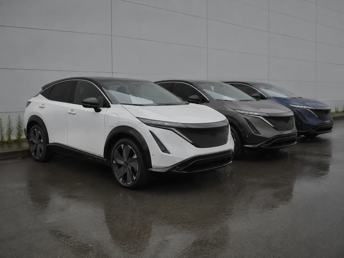 Three unsold Nissan Ariya electric crossovers parked in a row on a dealer forecourt under grey cloud - Nissan Ariya