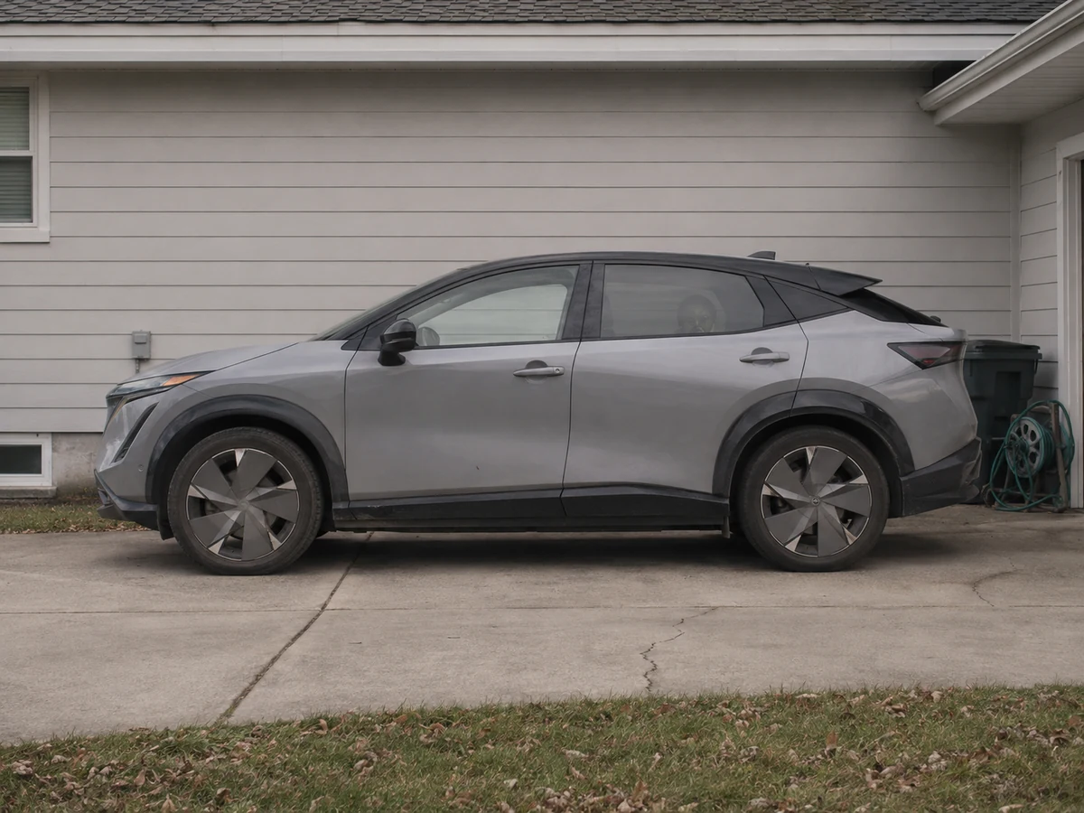 Three-year-old Nissan Ariya electric crossover in side profile on a suburban driveway with road film along the sills - Nissan Ariya