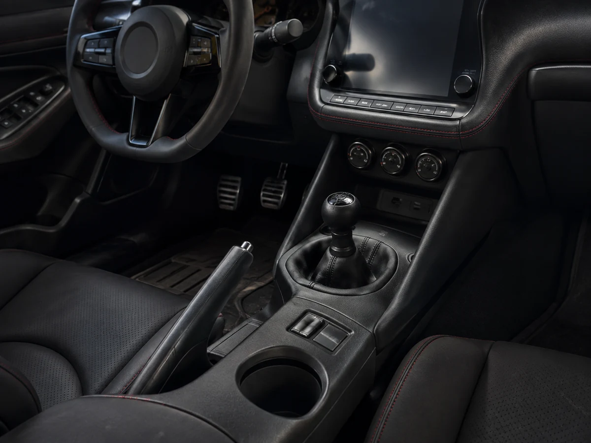 Six-speed manual gear lever and three pedals in a Nissan Z cabin with the driver's hand on the shift knob - Nissan Z