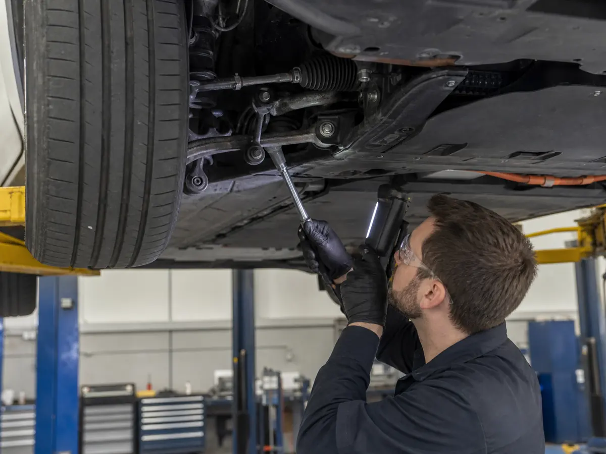 Technician checking electric sedan front suspension fasteners, tire wear, and steering joints - Tesla Model 3