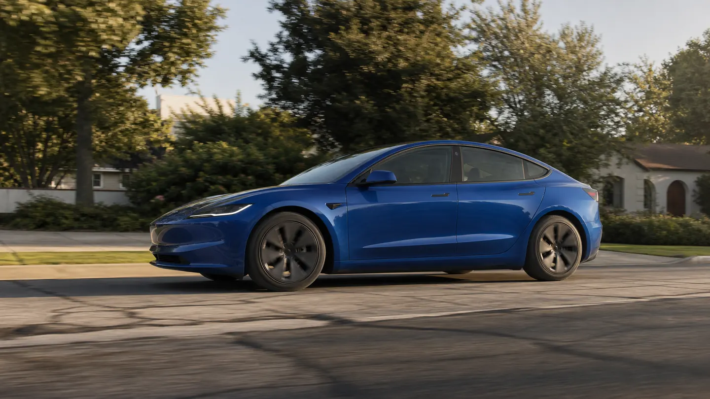 Tesla Model 3 driving over patched suburban pavement in a low side view