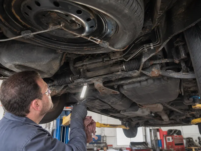 Technician inspecting an older minivan underbody and spare-tire carrier - Toyota Sienna